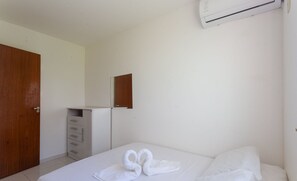A hotel room with a bed, a wooden door, a white dresser, and a wall-mounted air conditioner. - Townhouse 300m From Ilheus Beach Vcm005 (Ilhéus)