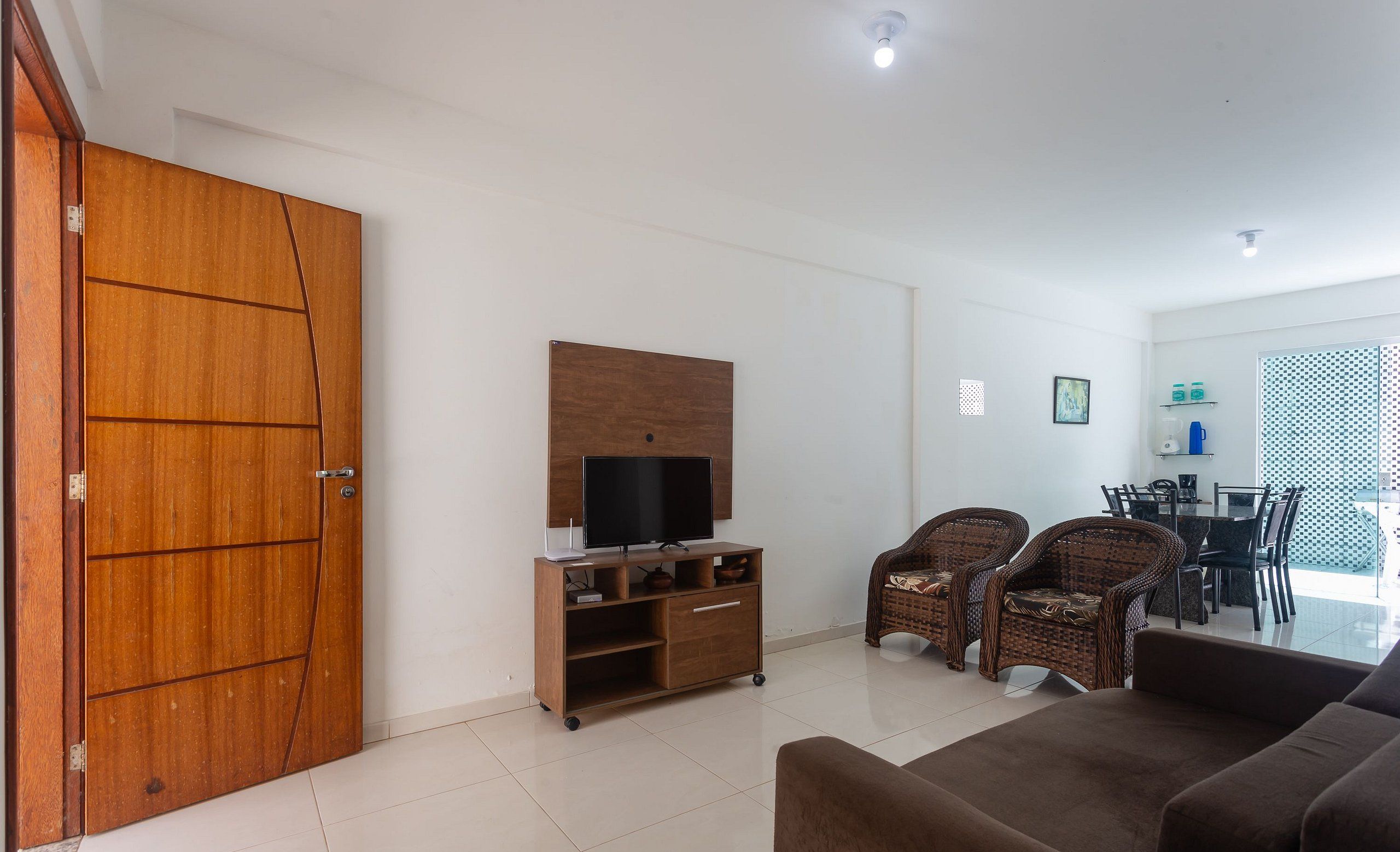 A living room with a sofa, wicker chairs, a TV stand, and a dining area with chairs and a table.