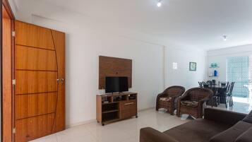 A living room with a sofa, wicker chairs, a TV stand, and a dining area with chairs and a table.