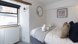 A bedroom with a bed, a window, a radiator, a mirror, and a framed picture on the wall. - Charming 3-Bed Cottage in Central Stroud (Gloucestershire)