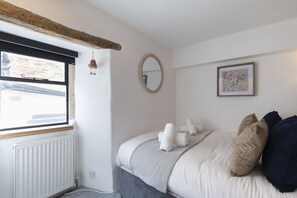 A bedroom with a bed, a window, a radiator, a mirror, and a framed picture on the wall. - Charming 3-Bed Cottage in Central Stroud (Gloucestershire)