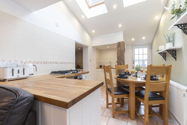 A modern kitchen with a central island, wooden dining table, and chairs. - Charming 3-Bed Cottage in Central Stroud (Gloucestershire)
