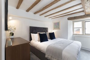 A bedroom with a bed, wooden beams, a nightstand, and a window.