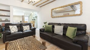 A living room with two dark leather sofas, a wooden coffee table, and a large mirror with a wavy frame. - Charming 3-Bed Cottage in Central Stroud (Gloucestershire)
