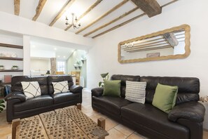A living room with two dark leather sofas, a wooden coffee table, and a large mirror with a wavy frame. - Charming 3-Bed Cottage in Central Stroud (Gloucestershire)