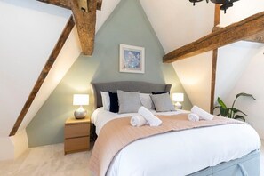 A bedroom with a sloped ceiling, a bed with a headboard, bedside tables with lamps, and a framed picture on the wall. - Charming 3-Bed Cottage in Central Stroud (Gloucestershire)