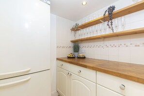 A kitchen with white cabinets, wooden countertops, and a shelf with wine glasses. - Charming 3-Bed Cottage in Central Stroud (Gloucestershire)