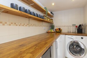 A kitchen with wooden shelves holding pots, a washing machine, and a fruit bowl.