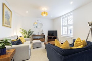 A modern living room with a sofa, ottoman, and a TV stand.