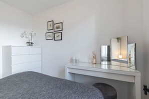 A modern bedroom with a bed, a dresser, a vanity with a mirror, and framed pictures on the wall.