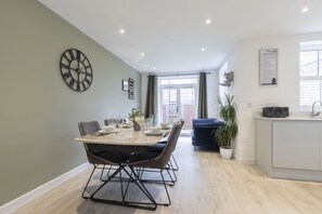 A modern kitchen with a dining area, featuring a large clock, a potted plant, and a view to the outside.