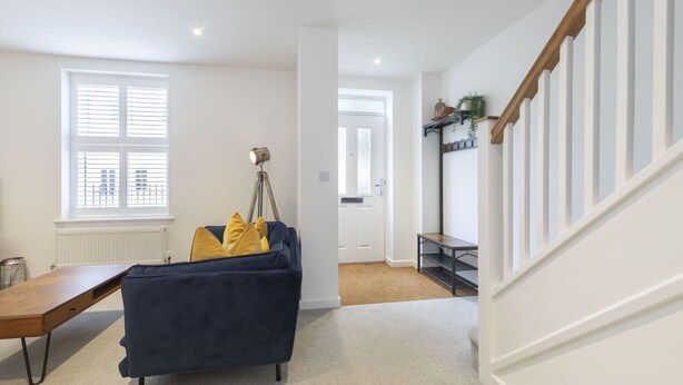 A modern living room with a dark blue sofa, a wooden coffee table, and a floor lamp. A staircase with a wooden railing leads to another room. - Stylish 2-Bed Home in Fairview with Free Parking (Gloucestershire)