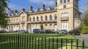 A row of terraced houses with a well-maintained lawn and a black metal fence in the foreground. - Stylish 2-Bed Home in Fairview with Free Parking (Gloucestershire)