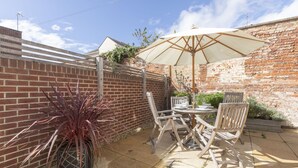 A patio with a brick wall, a wooden fence, and a table with chairs and an umbrella. - Stylish 2-Bed Home in Fairview with Free Parking (Gloucestershire)
