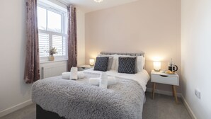 A bedroom with a large bed, a bedside table with a lamp, and a window with curtains. - Stylish 2-Bed Home in Fairview with Free Parking (Gloucestershire)