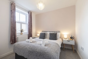 A bedroom with a large bed, a bedside table with a lamp, and a window with curtains. - Stylish 2-Bed Home in Fairview with Free Parking (Gloucestershire)