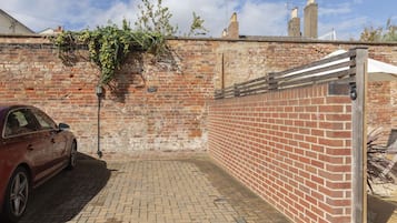 A brick wall with a metal gate, a red car parked on a brick pavement, and a brick building in the background.