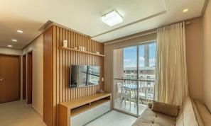 A modern living room with a flat-screen TV, wooden paneling, a sofa, and a balcony with a view.