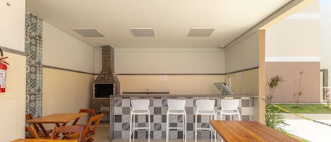 An outdoor patio with wooden tables and chairs, a brick-built barbecue grill, and a tiled backsplash.