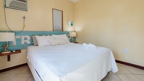 A hotel room with a bed, a nightstand, a wall-mounted air conditioner, a wall-mounted light, and a framed picture. - Beautiful House With Pool & Barbecue Ura0015 (Porto Seguro)