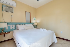 Ein Hotelzimmer mit Bett, Nachttisch, Wandklimaanlage, Wandleuchte und einem gerahmten Bild.