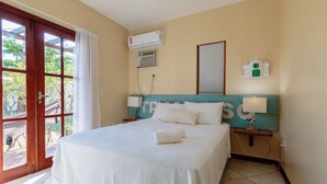 A hotel room with a bed, a window with curtains, an air conditioning unit, a wall-mounted clock, and a small table with a lamp. - Beautiful House With Pool & Barbecue Ura0015 (Porto Seguro)