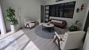 A modern living room with a sofa, two armchairs, a coffee table, and a large window.