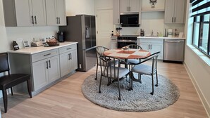 A modern kitchen with grey cabinets, a stainless steel refrigerator, a microwave, and a dishwasher. There is a dining table with chairs and a rug in the center.