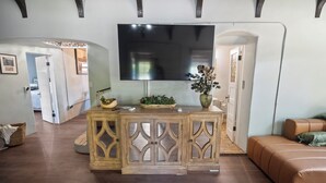 A living room with a large flat-screen TV mounted on a wooden console, a brown leather sofa, and a decorative plant.