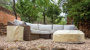 A sectional sofa with a chaise, a covered ottoman, and a wicker chair set on a gravel surface.