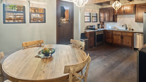 A wooden dining table with chairs, a chandelier, and a kitchen with wooden cabinets and a dishwasher.