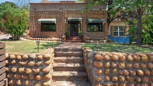A stone building with a staircase leading to a door, surrounded by stone walls and greenery.