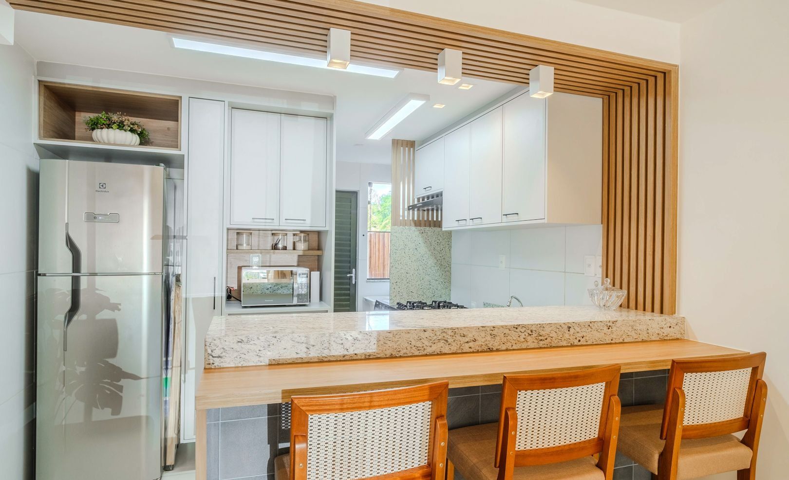 A modern kitchen with white cabinets, a stainless steel refrigerator, a microwave, and a wooden dining table with chairs.