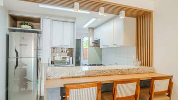 A modern kitchen with white cabinets, a stainless steel refrigerator, a microwave, and a wooden dining table with chairs.