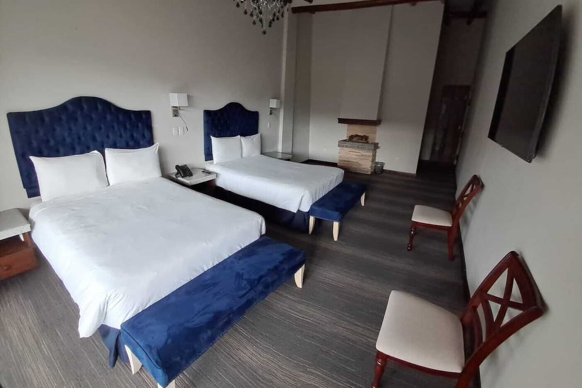A hotel room with two beds, a desk, a chair, and a small table.