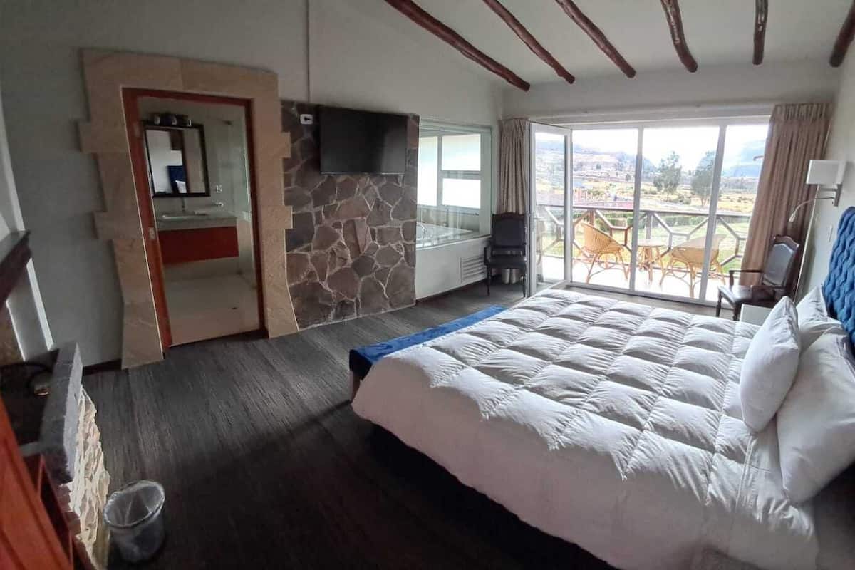 A bedroom with a large bed, stone wall, and a view of the outdoors.