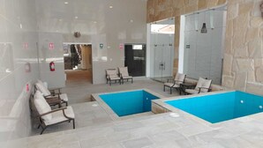 Area piscina con due piscine, sedute e un muro in pietra.