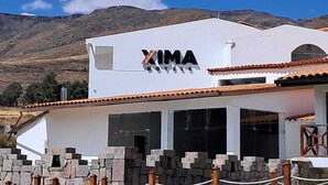 Un edificio bianco con il cartello "XIMA HOTELS" sul lato, circondato da mura in pietra e con montagne sullo sfondo.