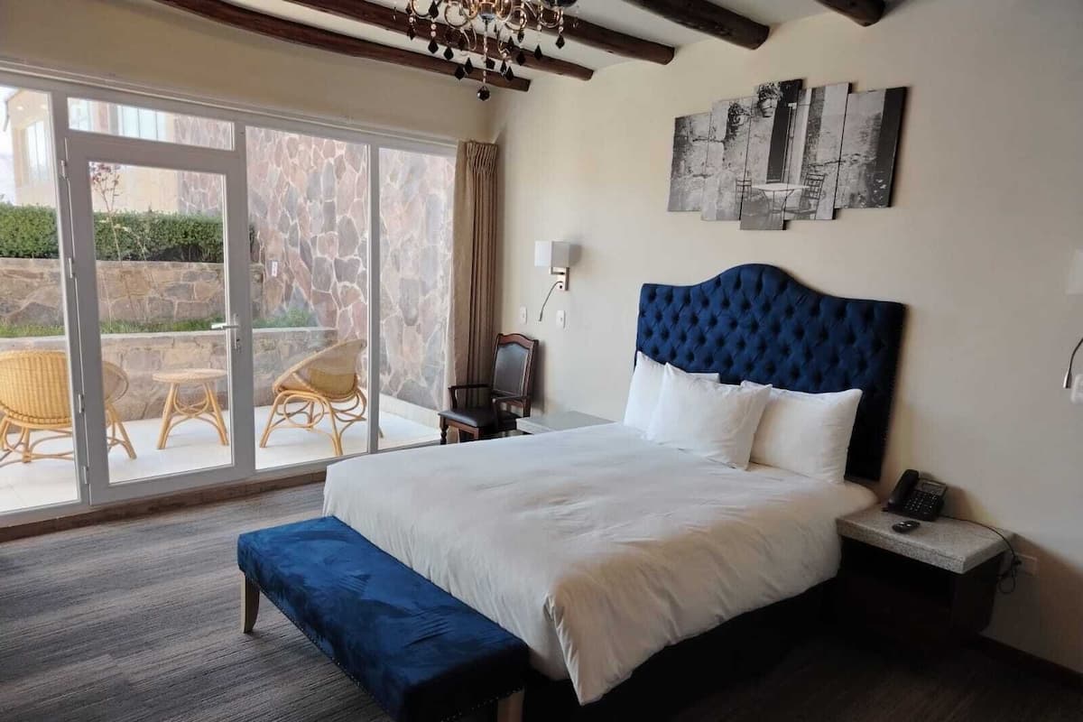 A bedroom with a large bed, a bench, a nightstand with a phone, and a view of the outdoors through a glass door.