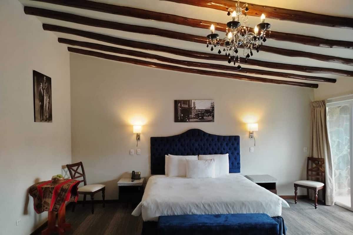 A hotel room with a large bed, two bedside tables, a chandelier, and a view of the outdoors.