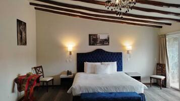 A hotel room with a large bed, two bedside tables, a chandelier, and a view of the outdoors.