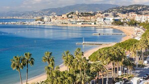 A coastal cityscape with a beach, palm trees, and a marina. - Sublime appartement à 100m de la Croisette (Cannes)
