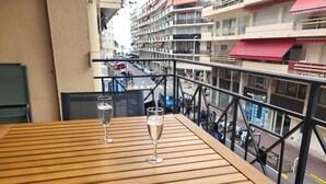 A wooden table with two glasses of champagne on a balcony overlooking a street with parked cars and buildings. - Sublime appartement à 100m de la Croisette (Cannes)