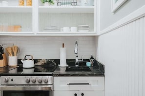 Una cocina con armarios blancos, encimera negra, estufa y lavabo.