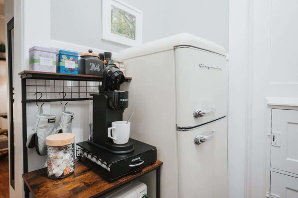 A kitchenette with a coffee machine, a jar of sugar, and a white refrigerator. - Historic Downtown Condo| Prime Location| Walkable (Savannah)