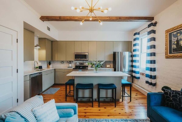 A modern kitchen with a central island, wooden beams, and a striped curtain.