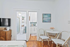 A room with a bed, a TV, a wooden cabinet, a white wall, a painting, and a door leading to a bathroom.
