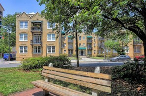 A multi-story brick building with balconies, a green awning, and a bench in the foreground. - Darling Downtown Renovated Historic Condo | Walkable (Savannah)