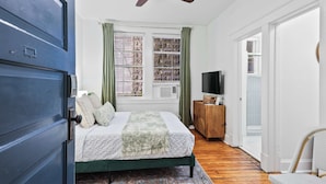 A bedroom with a bed, a ceiling fan, a TV, and a wooden cabinet.