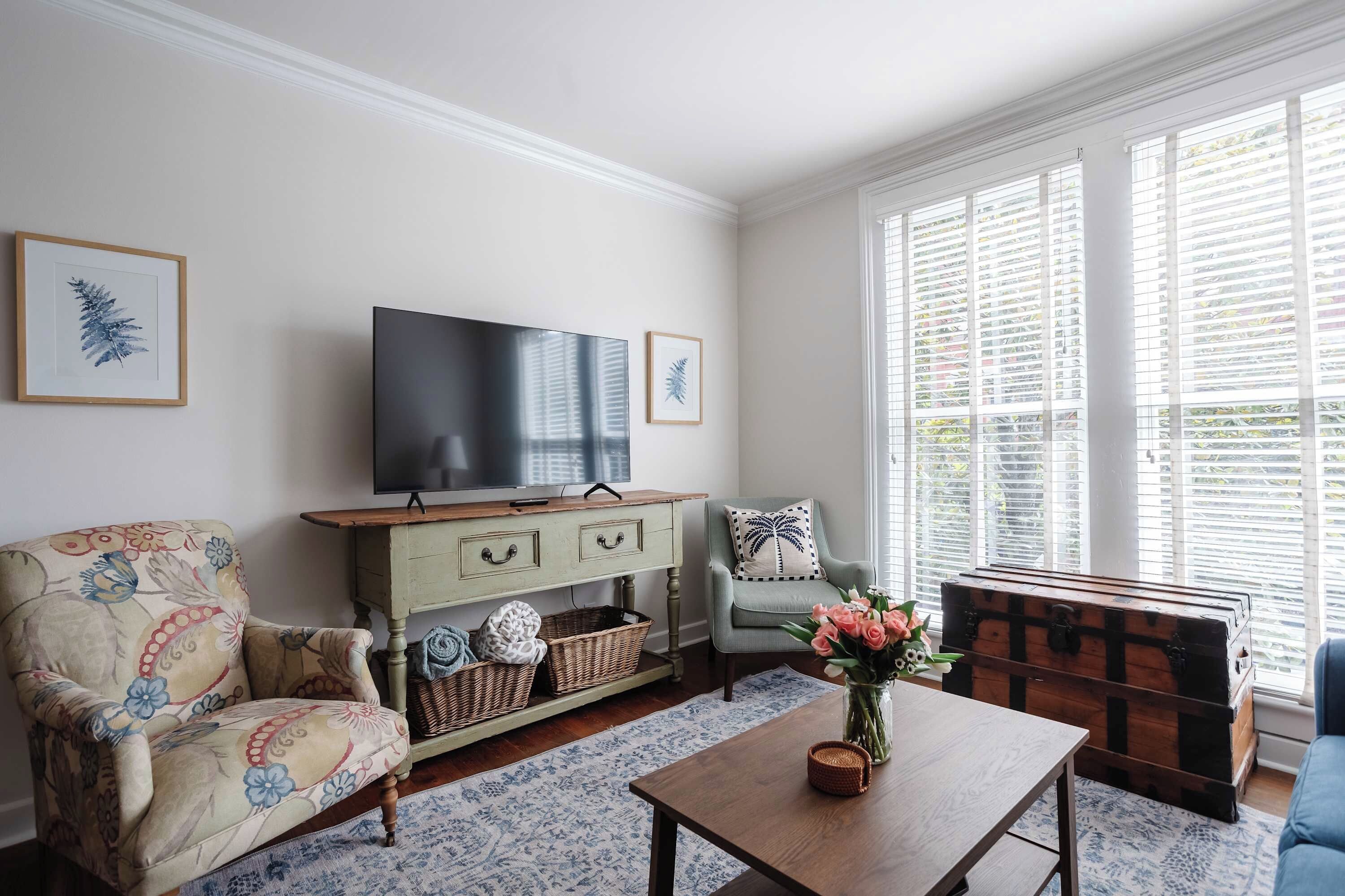A living room with a television, a sofa, a chair, a coffee table, and a window with blinds.